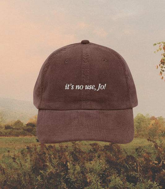 May include: A brown corduroy baseball cap with the text "it's no use, Jo!" embroidered in white on the front.