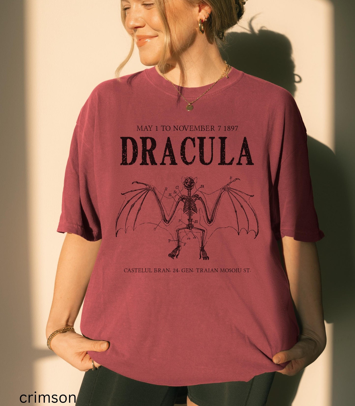 May include: Crimson-colored t-shirt featuring the word "DRACULA" in a distressed font, with the dates "MAY 1 TO NOVEMBER 7 1897" above it. Below is a skeletal bat illustration. The text "CASTELUL BRAN 24 GEN TRAIAN MOSOIU ST" is at the bottom.