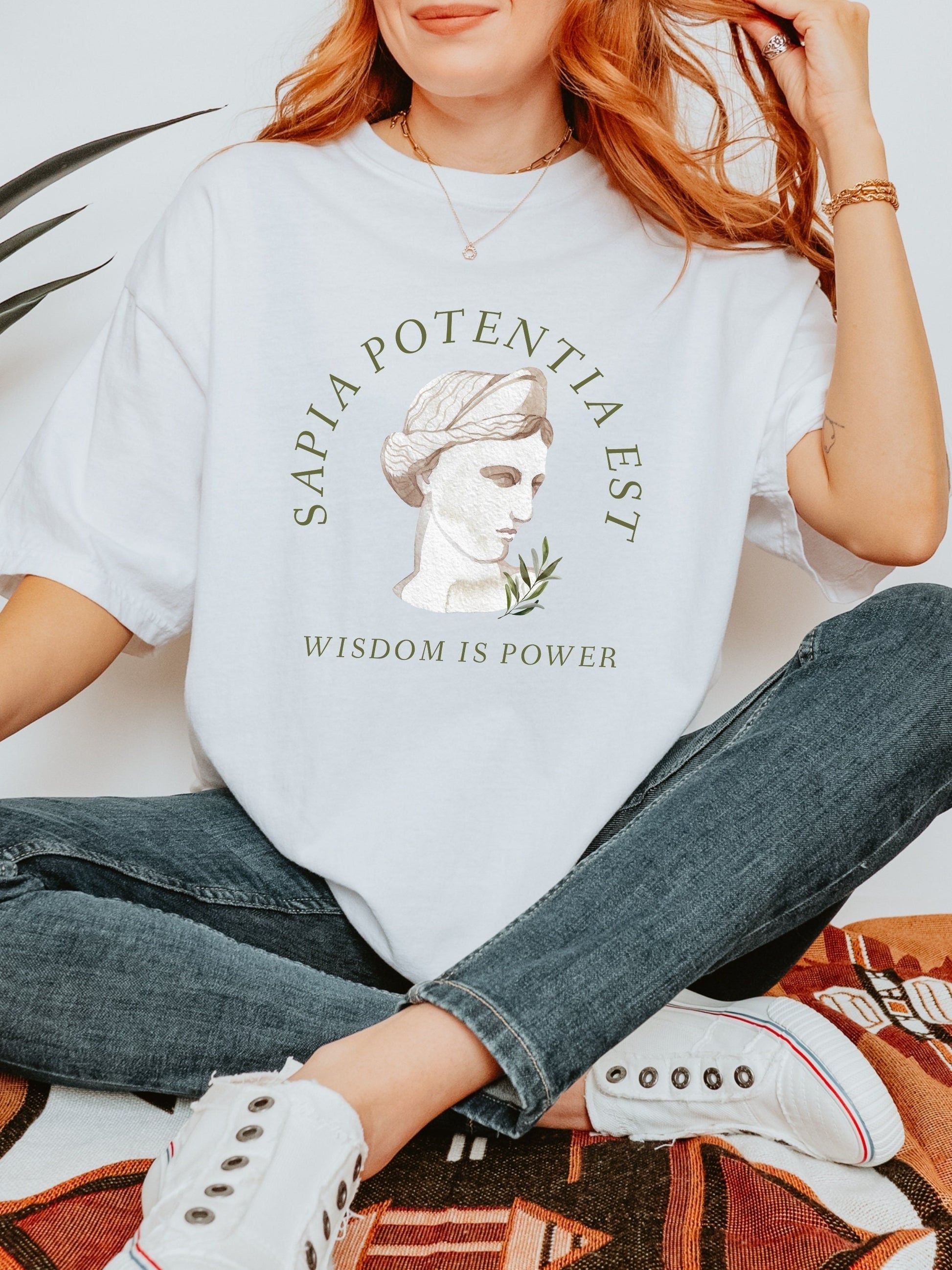 May include: White t-shirt with a green graphic of a woman's bust with the text "SAPIA POTENTIA EST" and "WISDOM IS POWER" below.