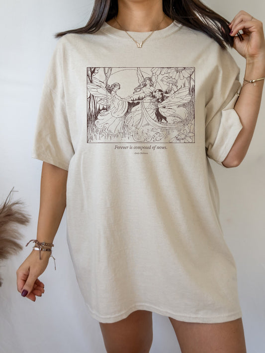 May include: A beige oversized t-shirt with a vintage illustration of three fairies with wings and the text "Forever is composed of nows. - Emily Dickinson" printed on the front.